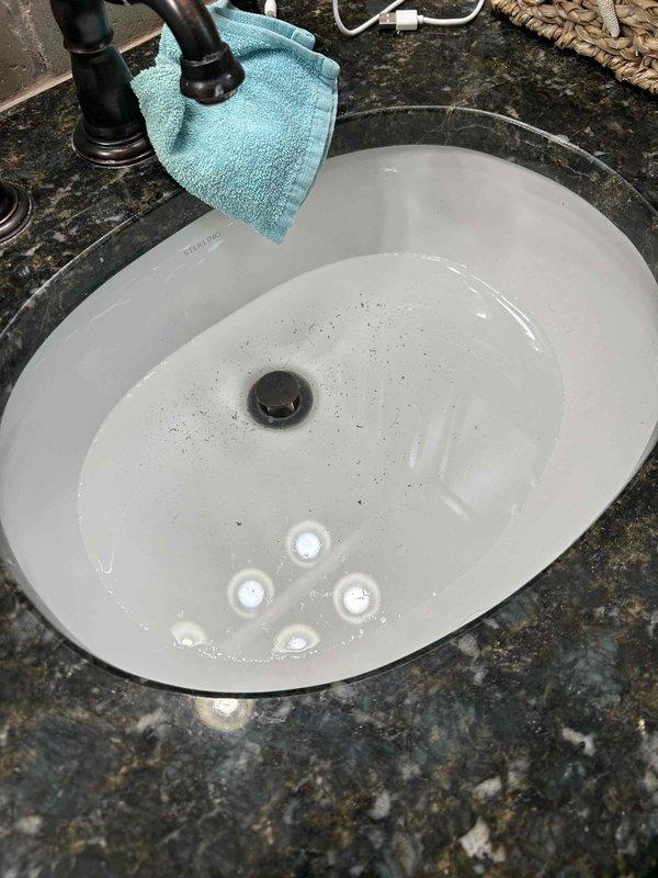 Responded to drainage issue at residential property with three HVAC systems, main system located in attic of 19-year-old home. Upon arrival, found bathroom sink basin with standing water and visible debris, indicating drainage obstruction. Inspected under-sink plumbing configuration and identified slow drain condition in P-trap assembly. Cleared blockage from white PVC drain pipes and P-trap using appropriate tools and techniques. Verified proper water flow through drain system and confirmed chrome drain flange connection integrity. Tested drainage performance with multiple water flow cycles to ensure complete resolution of standing water issue. All plumbing components, including compression fittings and slip joints, inspected and confirmed in proper working condition upon completion.
