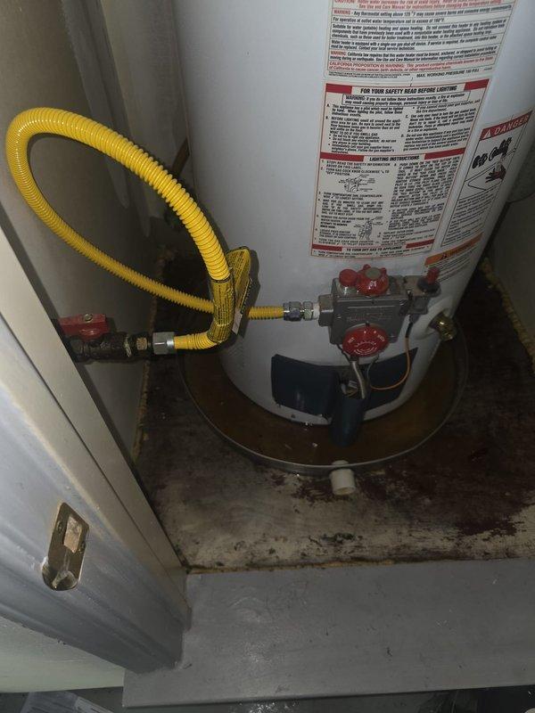 Responded to no hot water emergency at residential property with 20+ year old gas tank water heater actively leaking in garage. Upon inspection, confirmed tank failure with visible water damage on concrete floor beneath unit and compromised tank integrity. Evaluated existing gas line connection with flexible yellow corrugated connector and shut-off valve configuration. Assessed overall plumbing system including overhead pipe routing and insulation condition in utility area. Discussed water heater replacement options and provided consultation on water softener installation to address water quality concerns for the home's plumbing system.