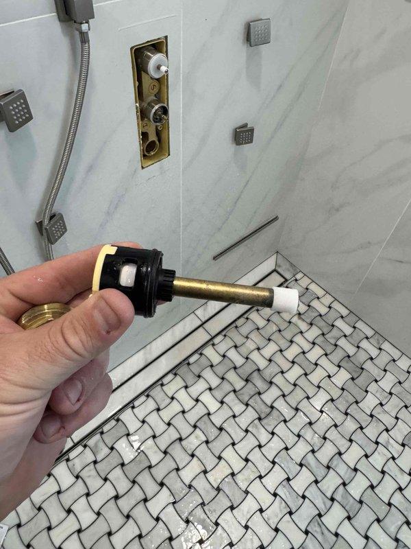 # Plumbing Service Completed

Responded to service call for low water pressure issue at 26-year-old residential property. Upon investigation, identified faulty shower valve cartridge as primary cause of reduced water flow. Removed deteriorated brass valve cartridge with worn rubber seal from shower mixing valve assembly. The cartridge showed significant age-related wear and mineral buildup affecting water flow regulation.

Inspected the exposed brass valve body in the marble-tiled shower enclosure and confirmed compatibility for replacement cartridge. Cleaned valve seat and surrounding connections to ensure proper seal. Installed new valve cartridge and tested shower system including handheld attachment and body spray jets for proper pressure restoration and temperature control.

Additionally inspected the home's water heating system consisting of one traditional tank water heater and two wall-mounted tankless units with expansion tank. Verified all equipment operating within normal pa