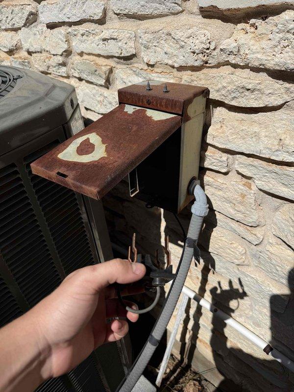 Responded to thermostat replacement request for single HVAC system with split configuration—air handler located in hallway closet and condensing unit positioned in attic. Performed diagnostic evaluation of existing thermostat and system controls to determine functionality and compatibility issues. Inspected outdoor condensing unit, noting advanced corrosion on compressor housing, significant rust deterioration on top panel components, and aging refrigerant line connections with visible mineral deposits and discoloration at valve assemblies. Documented equipment condition showing extensive wear consistent with system of unknown age in 1974 residence. Evaluated system operational parameters and provided recommendations for thermostat upgrade options compatible with existing split system configuration.