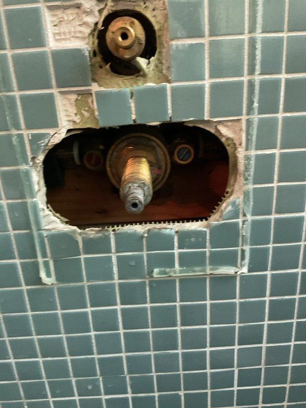 Responded to guest house shower temperature control issue where water randomly fluctuated between hot and cold. Diagnosed failed thermostatic cartridge in shower valve assembly. Removed tiled wall access panels to expose valve body and disassembled pressure-balancing cartridge system. Extracted defective blue thermostatic cartridge along with worn seals, O-rings, and retaining clip from brass valve housing. Installed new pressure-balancing cartridge assembly with fresh gaskets and seals, reassembled valve components, and tested for proper temperature regulation and consistent water flow.