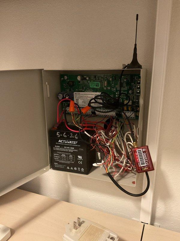 Assessed legacy security system control panel and wiring enclosure containing original circuit board, backup battery, and associated low-voltage wiring that was flagged for potential removal by security technician during new system installation. Verified that existing panel and wiring are no longer required for new security system operation and can be safely disconnected and removed. Removed wall-mounted security panel enclosure and disconnected all associated low-voltage wiring. Replaced burned-out bulb in pendant light fixture over stairwell using extension ladder to access elevated location.