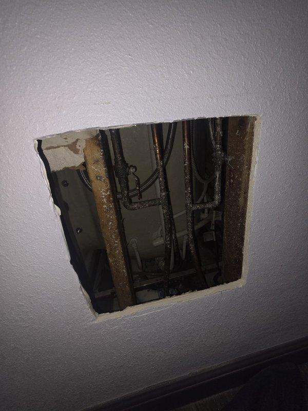 Responded to water leak complaint affecting bedroom wall with two bathrooms on opposite side. Performed exploratory access by cutting drywall to expose wall cavity and investigate source of water intrusion. Inspection revealed plumbing supply lines and electrical components within wall framing. Accessed wall cavity to assess moisture damage to carpet and flooring, and identified location of leak within concealed plumbing system for repair access.