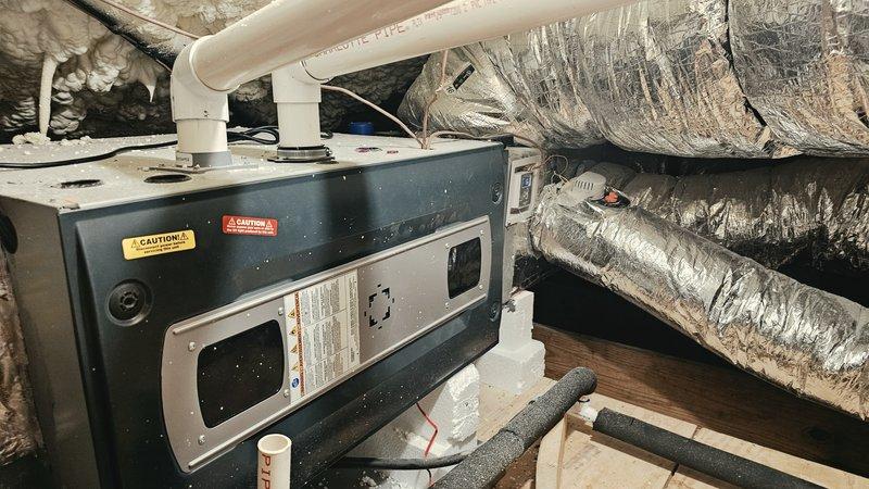 Responded to service call for 3-year-old residential HVAC system in attic not cooling and failing to maintain temperature. Accessed attic system using gate code, confirmed safe working conditions. Inspected air handling unit, condensate drain pan, drainage lines, and associated ductwork. Documented system condition including condensate management components, PVC drainage piping with brass fittings and shut-off valve, and flexible ductwork connections. Evaluated unit operation, checked refrigerant levels, and assessed airflow through silver flex duct system. System restored to proper cooling operation and temperature holding capability.