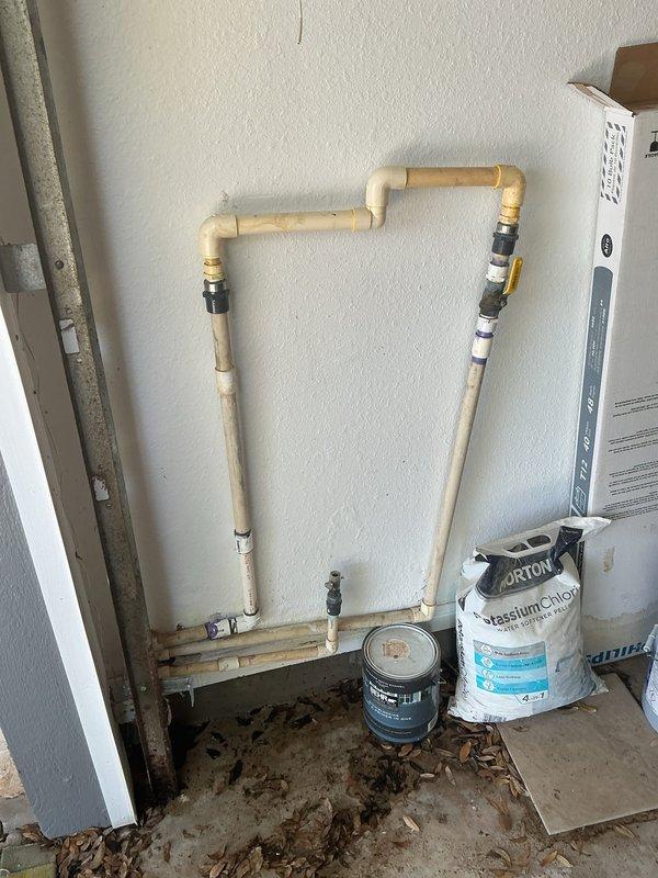 Responded to an active water leak at a garage pressure gauge assembly. Upon arrival, found water actively dripping from a brass threaded fitting at the wall connection point where a pressure gauge was mounted. The gauge displayed significant weathering and corrosion on the chrome finish, and a puddle had formed on the concrete floor beneath the fixture. 

Inspected the CPVC plumbing system configuration on the adjacent wall, which included vertical and horizontal pipe sections connected by elbow joints with black rubber coupling connectors. Given the home's age and the condition of the pressure gauge assembly, determined that the leak originated from a failed seal at the threaded connection between the brass fitting and the wall-mounted pipe. 

Shut off water supply to the affected line and removed the deteriorated pressure gauge. Cleaned the threaded brass fitting and inspected for damage or corrosion that could prevent proper resealing. Applied appropriate thread sealant and reinstal