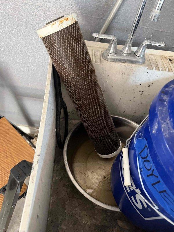 Responded to service call for water softener filter replacement at 2002-built residential property. Assisted homeowner with procurement and installation of replacement filter cartridge for water softening system. Removed heavily discolored and saturated filter element from housing unit, indicating proper filtration function and need for scheduled replacement. Installed new filter cartridge into existing wall-mounted softener system with black insulated piping configuration. Verified proper seating of filter housing, checked system connections for leaks, and restored water flow through softener loop. System returned to normal operation with improved water quality expected.