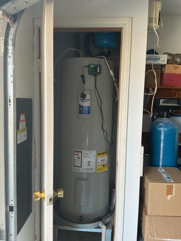 Performed member maintenance inspection at residential property. Investigated reported toilet leak with suspected wax ring failure. Upon inspection, identified water damage and staining on bathroom wall behind toilet near water supply line connection point, indicating active or previous leak at supply line rather than wax ring. Documented condition of toilet installation and surrounding areas. Conducted visual inspection of water heater system located in garage, confirming electric tank-type unit with standard safety labeling, expansion tank, and copper supply connections in serviceable condition. Photographed plumbing fixtures and conditions for maintenance records.