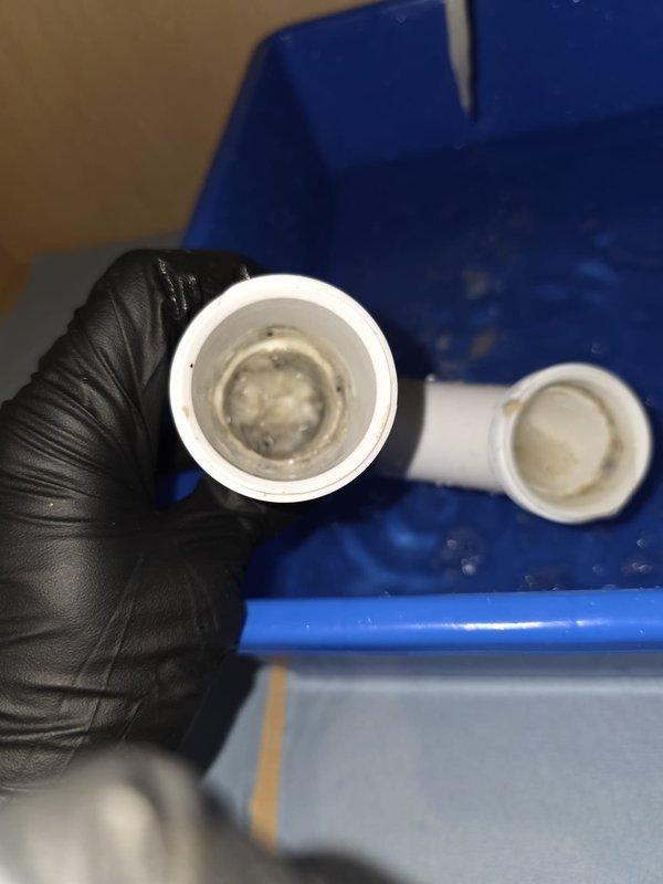 Responded to ongoing clogged sink issue in upstairs bathroom. Upon inspection, discovered severe mineral buildup and scaling within the PVC drain piping causing restricted flow. Disassembled P-trap assembly and elbow fittings, revealing significant calcium and sediment deposits accumulated on interior pipe walls. Removed affected sections of drain line and thoroughly cleaned all components. Replaced compromised fittings with new PVC connections to restore proper drainage. Tested system to confirm full flow restoration and proper operation of sink drain.