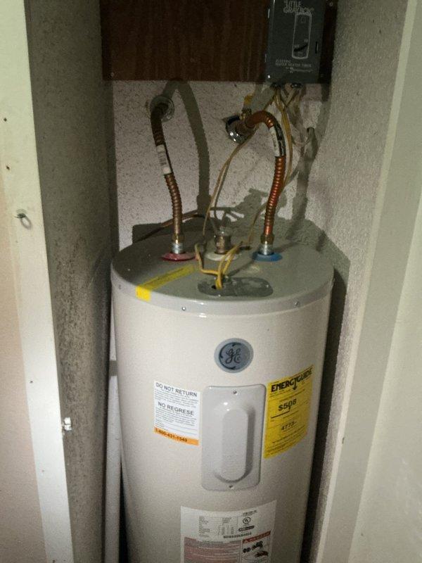 Responded to active leak on GE water heater. Upon arrival, inspected unit and water supply connections at top of heater where flexible braided supply lines connect to domestic water system. Identified source of leak and performed necessary repairs to stop water discharge. Verified all connections at water heater, including hot and cold supply lines with red and blue fittings, were properly secured. Inspected associated plumbing system including PVC piping configuration with multiple shut-off valves and blue water filter housing to ensure no additional leaks present. Tested system operation and confirmed leak was resolved with no further water discharge observed.