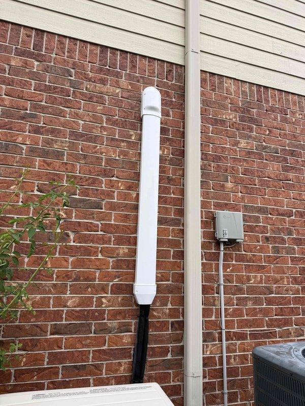Completed installation of new 18,000 BTU Mitsubishi mini-split system on residential brick and vinyl siding exterior. Mounted outdoor condenser unit at ground level, installed refrigerant line set and electrical disconnect box on exterior wall, and routed condensate drainage through white PVC piping along brick facade. System includes comprehensive 12-year parts and labor warranty coverage.