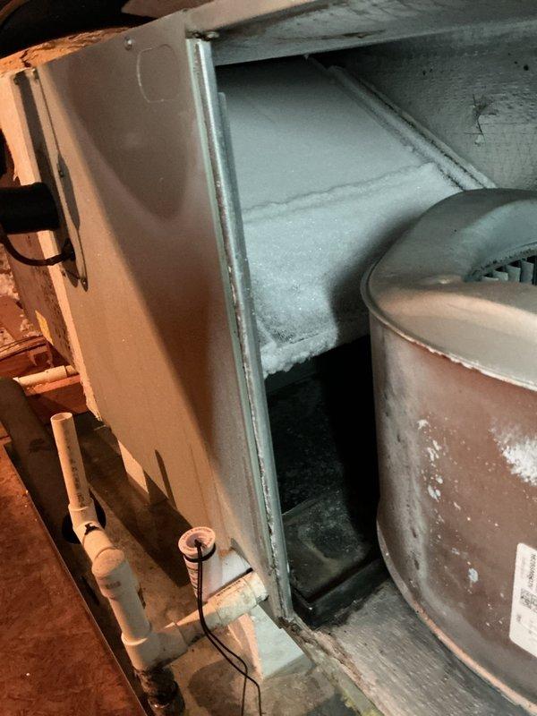 Responded to emergency drain issue at residential property with 3,155 square foot home containing approximately 5-year-old HVAC system. Upon inspection, discovered extensive ice accumulation on evaporator coils and internal components of air handler unit located in attic space. Heavy frost buildup observed throughout coil surfaces indicating restricted airflow and potential drainage complications. Blower motor assembly exhibited significant dust and debris accumulation on wheel fins and internal surfaces, contributing to reduced system efficiency and airflow restriction. Documented moisture staining and condensation on cylindrical blower housing and surrounding drain lines. Photographed frozen evaporator coils and contaminated blower assembly for records. System required immediate attention to address ice formation, clear drain blockage, and restore proper operation. Recommended thorough cleaning of blower assembly and evaluation of drain line functionality once system defrosted.