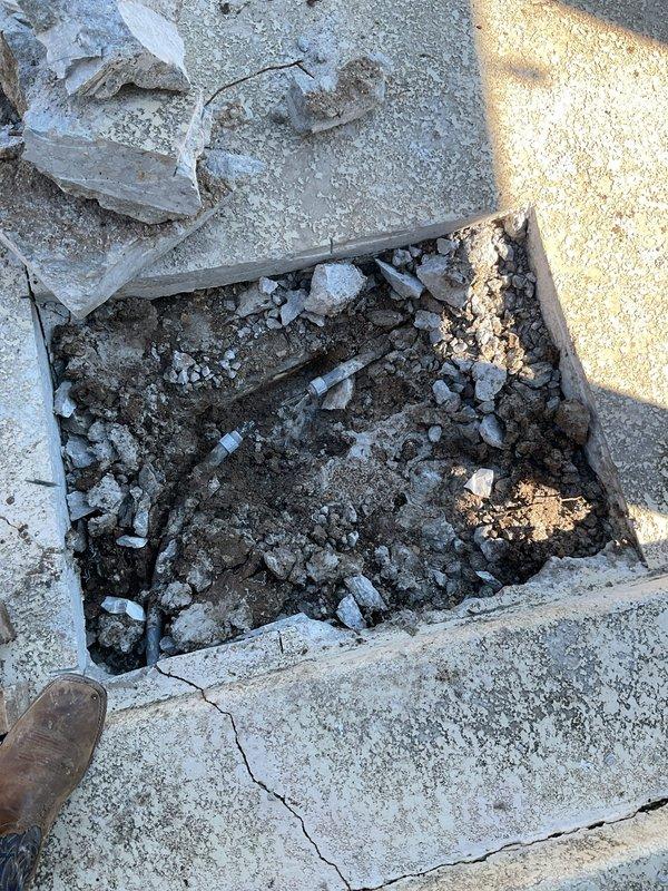 Excavated and accessed underground drainage system through concrete pavement to service existing sump basin. Removed deteriorated concrete sections and exposed subsurface utilities including PVC piping components. Cleared debris from white plastic drain basin, addressed standing water accumulation, and inspected coiled drainage line within the sump pit to ensure proper functionality.