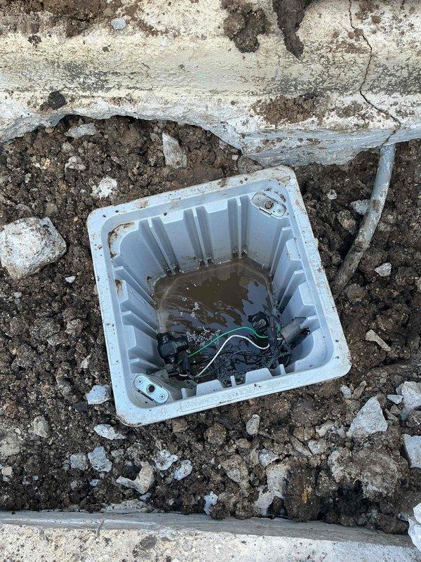 Excavated and accessed underground drainage system through concrete pavement to service existing sump basin. Removed deteriorated concrete sections and exposed subsurface utilities including PVC piping components. Cleared debris from white plastic drain basin, addressed standing water accumulation, and inspected coiled drainage line within the sump pit to ensure proper functionality.