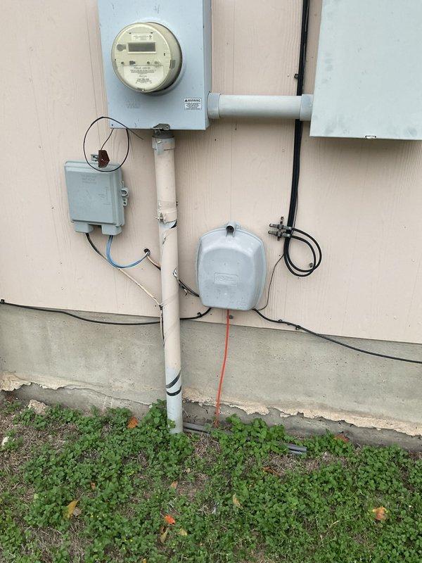Inspected the exterior service entrance and found the meter can conduit (riser) detached from the meter enclosure, with visible scuffing, cracking, and weathering along the vertical conduit run. Documented the condition of the main panel, which is properly labeled with main, range, dryer, furnace, air conditioner, and water heater breakers and shows no signs of rust, moisture intrusion, or breaker damage. The detached riser was identified as a repair item requiring correction to restore a secure, code-compliant connection at the meter can.
