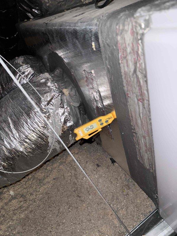 Performed member maintenance inspection on the attic-mounted HVAC system, including electrical measurements at the air handler (blower motor amp draw recorded at 0.38 A) and verification of gas line, PVC condensate drain, and wiring connections with no frost, ice, rust, or visible damage observed. Inspected attic ductwork and identified torn and peeled foil-faced insulation on the rectangular duct board, exposing fiberglass insulation; surface temperature of approximately 104°F was measured at the duct, and the damaged insulation facing is recommended for repair to restore thermal and vapor barrier integrity.
