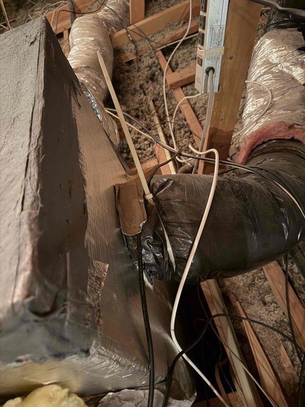 Performed an on-site evaluation of the attic duct system to provide a replacement estimate for the existing flexible ductwork. Inspection found flex duct jackets torn open at a Y-branch junction with exposed fiberglass insulation and foil liner, temporary tape repairs, crinkled and loosely bunched vapor-barrier wrap at plenum connections, and weathered, worn insulation on the rectangular plenum. Documented conditions with photos, noting loose wiring and debris throughout the attic, and prepared the findings for a duct replacement proposal.