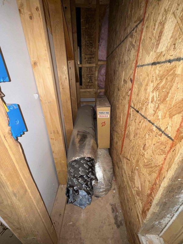 Accessed the unfinished attic/chase area via ladder to reach elevated ductwork requiring sealing. Inspected the flexible insulated duct runs and connections in the tight, framed passage and identified joints and connections needing air-leak remediation. Sealed duct connections to reduce conditioned air loss and improve system efficiency and airflow delivery. Noted stored rolls of insulated flex duct and construction debris in the work area; area left in working order following the repair.