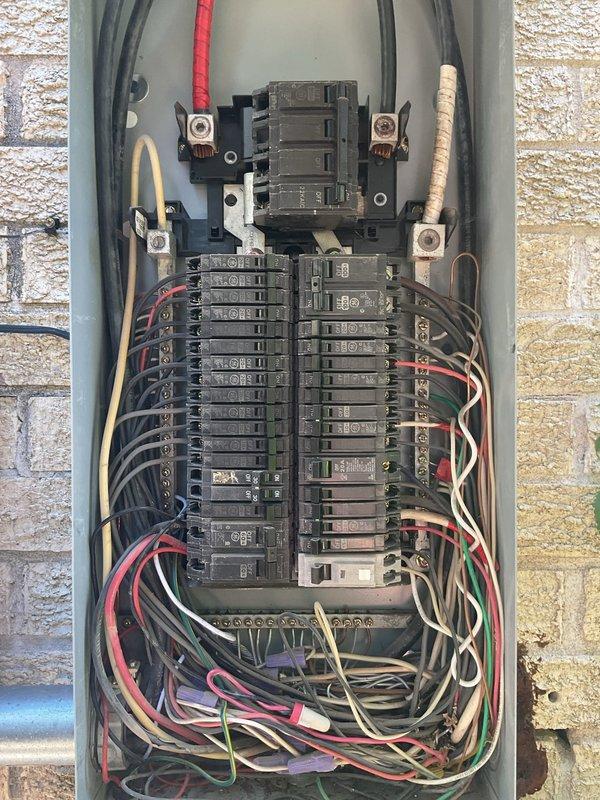 Evaluated the exterior-mounted electrical service, including the overhead service entrance, galvanized conduit riser, meter base, and main breaker panel, for the addition of three 220V garage outlets. Inspected the existing panel and found congested, loosely arranged conductors with multiple wire-nut splices, along with rust staining on the brick below the enclosure, and determined that a new panel and dedicated circuits are needed to support the added load. Prepared estimates for a panel replacement and for the branch wiring required for the planned mini-split system.