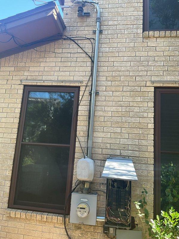 Evaluated the exterior-mounted electrical service, including the overhead service entrance, galvanized conduit riser, meter base, and main breaker panel, for the addition of three 220V garage outlets. Inspected the existing panel and found congested, loosely arranged conductors with multiple wire-nut splices, along with rust staining on the brick below the enclosure, and determined that a new panel and dedicated circuits are needed to support the added load. Prepared estimates for a panel replacement and for the branch wiring required for the planned mini-split system.
