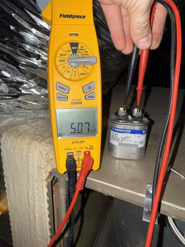 Responded to a no-heat call with cold air at the registers on an attic-installed furnace. Inspected the control board and low-voltage wiring and tested the run capacitor with a clamp meter, measuring 5.07 µF against a 7.5 µF rating, which is outside tolerance and indicates a weak capacitor. Observed dust buildup and disorganized, loosely routed wiring in the control compartment.