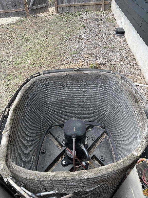 Performed member maintenance inspection on the outdoor condenser unit, removing the top grille and fan assembly to access the interior. Found the condenser coil fins heavily clogged with matted dust and lint buildup, restricting airflow and reducing heat transfer efficiency. The coil was cleaned to remove the debris, and the compressor, refrigerant lines, and wiring were visually inspected with no issues noted.