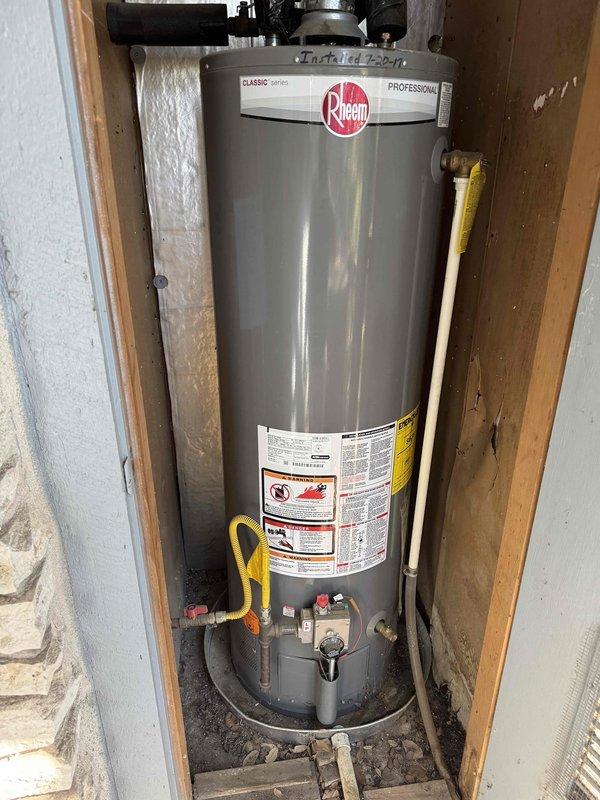 Responded to a leak at the washer connection in the middle bathroom and isolated it by shutting off the water supply to stop the leak. Documented the gas water heater (Rheem Classic Series, installed in a drain pan, handwritten install date on tank) and an electric point-of-use water heater under a countertop, recording system condition for the property's service history.
