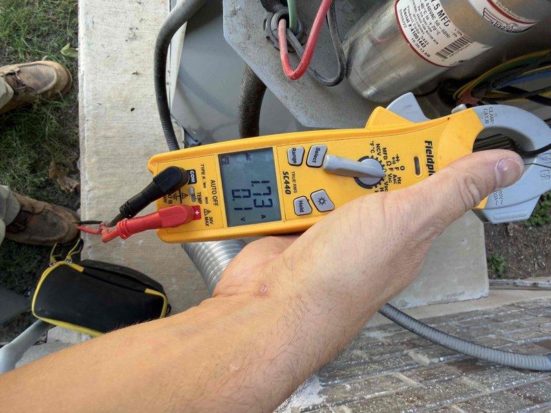 Responded to a no-operation call on a 6-year-old split system with the furnace and air handler located in the attic. Inspected the furnace area and found dark soot-like staining and charring on the foam-insulated line at the furnace base, along with debris and spray foam residue around the condensate and PVC piping. Performed electrical diagnostics at the outdoor condenser using a true RMS clamp meter, measuring amperage draw at the electrical compartment and inspecting the run capacitor and associated wiring. Documented findings with photos for review and follow-up recommendations.
