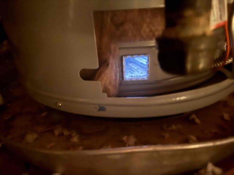 Inspected the attic-mounted A.O. Smith ProLine gas water heater and verified the pilot and burner were lit, with a steady blue flame visible through the combustion chamber viewing window. Evaluated the unit's operation, gas supply, vent, and drain pan, and identified the water heater that still requires the second anode rod so the outstanding component from the prior visit can be installed.