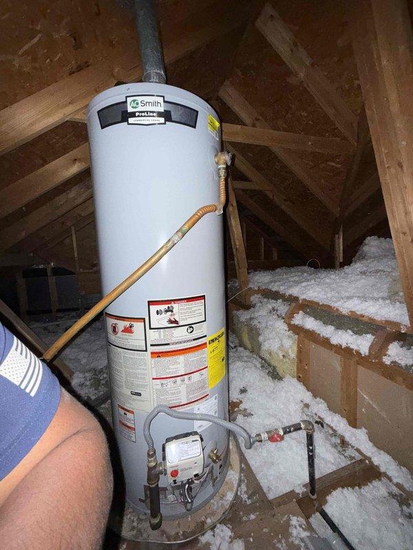 Inspected the attic-mounted A.O. Smith ProLine gas water heater and verified the pilot and burner were lit, with a steady blue flame visible through the combustion chamber viewing window. Evaluated the unit's operation, gas supply, vent, and drain pan, and identified the water heater that still requires the second anode rod so the outstanding component from the prior visit can be installed.