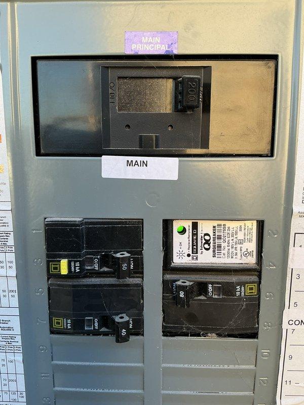 Inspected the main electrical panel (Square D, 200A main breaker) to evaluate power availability for a customer-supplied Google Nest floodlight camera at the rear/side exterior of the home. Verified the main breaker and installed Square D QO surge protection breaker, and observed discoloration near the white conductor termination at the main lug that warrants further evaluation. Documented panel conditions, including available breaker capacity and blanking plates covering unused positions, to support planning of the exterior camera circuit installation.