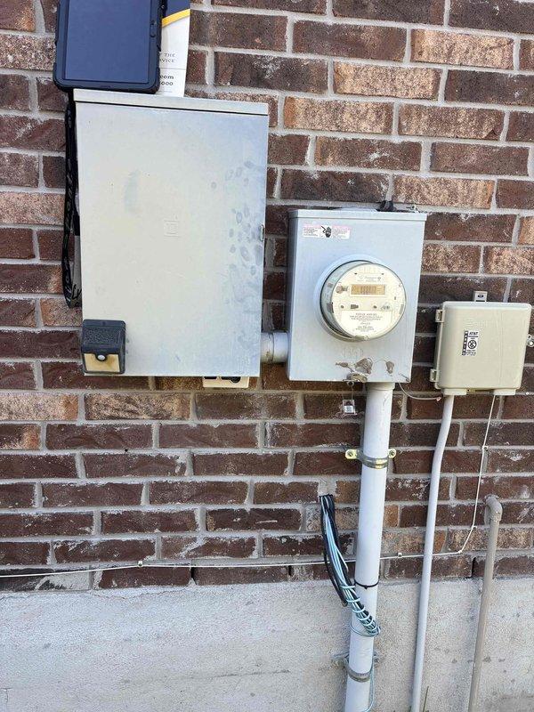Evaluated the electrical service for the requested exterior garage light installation, including inspection of the main breaker panel with the cover removed and the exterior service entrance equipment (meter base, disconnect enclosure, conduit, and telecommunications box) to assess available capacity and routing for the new circuit. The panel and exterior equipment were documented with photos, with no major damage noted, and the installation scope was reviewed for the exterior lighting.
