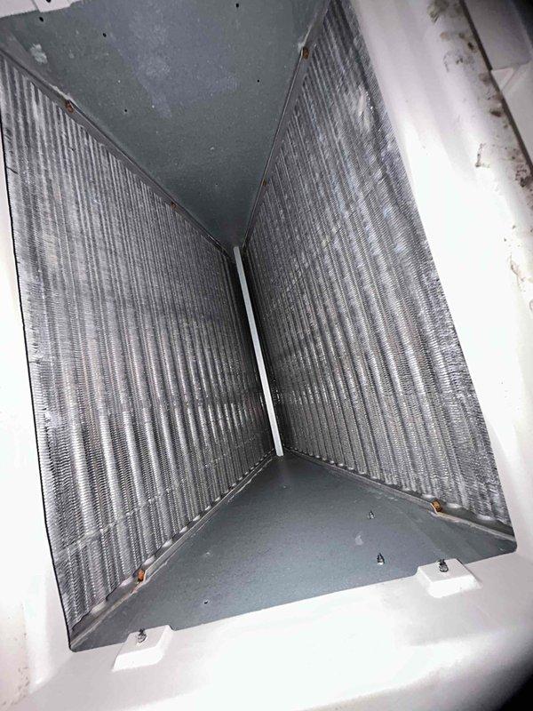 Responded to a no-airflow complaint with loud operating noise on a single attic-mounted split system. Inspection of the air handler showed a dust-laden A-coil with light surface rust on the coil frame fasteners, and a condensate drain line clogged with fibrous debris at the tee/access fitting. The blockage is the likely cause of the system shutdown and restricted operation, and the drain line and pan need to be cleared to restore proper condensate drainage.