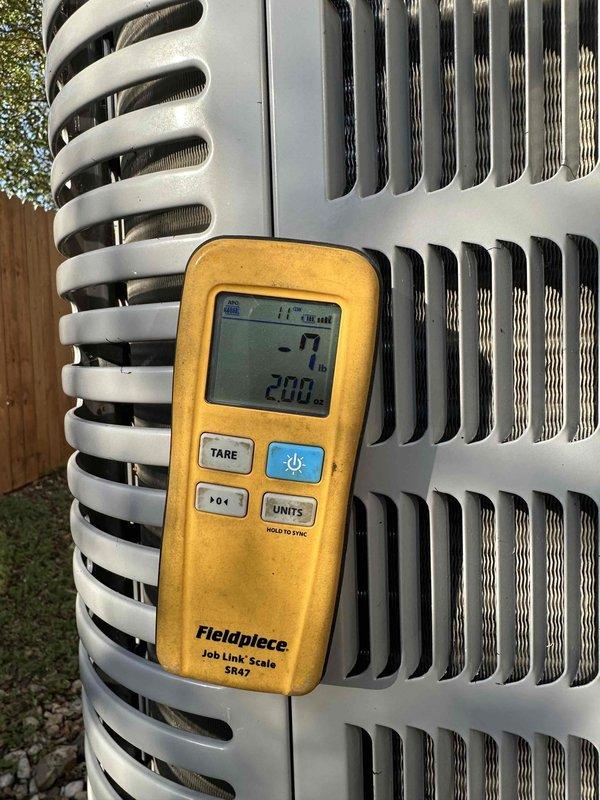 Performed warranty service on the outdoor condensing unit using a Fieldpiece Job Link SR47 refrigerant scale to measure refrigerant weight during charge adjustment. Tared the scale and monitored recovered/added refrigerant quantities to verify the system was brought to the correct charge specification.