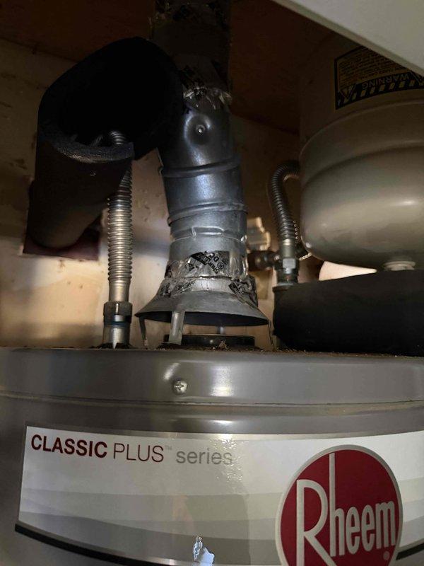 Responded to a no-hot-water call and found the pilot light out on the 7-year-old Rheem Classic Plus tank water heater, with nearby gas service interruptions reported following municipal work on a main gas line. Inspected the unit and its flue/vent connection, which showed dents and deteriorated foil tape at the draft hood joint, and noted the water softener and expansion tank installed on the system. Documented findings for the customer and recommended addressing the vent connection to ensure safe, reliable operation.