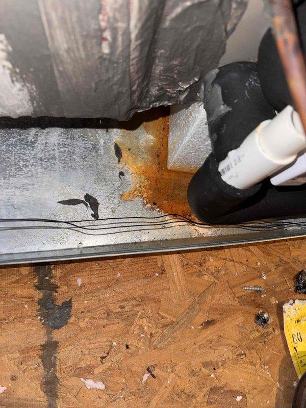 Inspected the attic-mounted air handler and reported duct leak, finding the secondary drain pan and base showing rust staining and corrosion near the line set and condensate drain connections, with sealant applied along the pan seam and no active leakage observed. Verified the electrical supply at the disconnect with a clamp meter to confirm proper operation of the system. Documented the rusted drain pan condition and the duct sealing for follow-up evaluation.