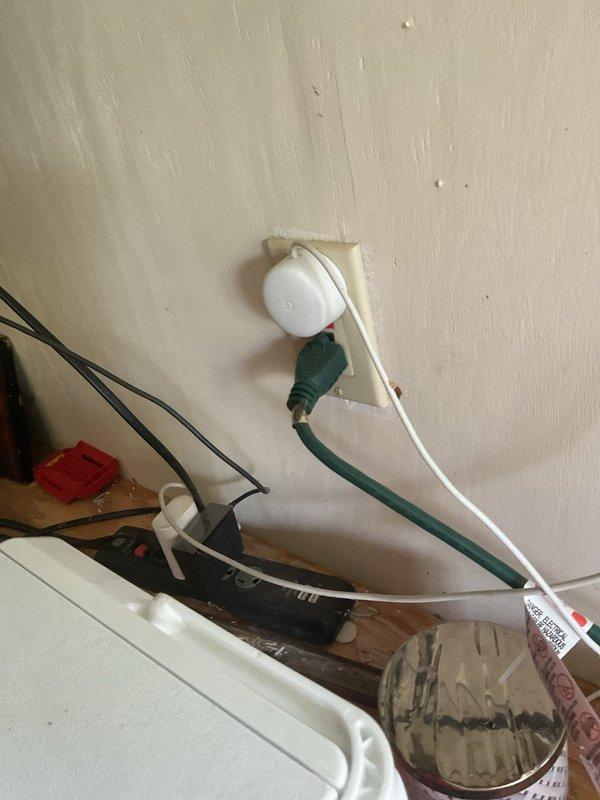 Performed an electrical maintenance inspection on a 50-year-old residence with three breaker boxes (two exterior, one interior). Opened and visually inspected the exterior panel enclosure, meter enclosure, and disconnect/meter socket assembly, evaluating conduit connections, breaker condition, and internal wiring and terminations. Also inspected the workshop receptacles, noting a power strip and extension cord plugged into the outlet and stored materials with hazard labeling nearby.
