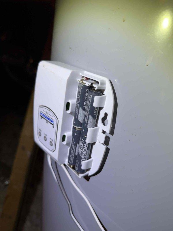 Responded to a no-hot-water complaint and inspected the 16-year-old gas tank-style water heater located in the attic. Evaluated the unit's operation, vent connections, and the installed FloodStop automatic leak-detection shutoff device, including its battery compartment and control status, to diagnose the loss of hot water to the kitchen and upstairs fixtures.