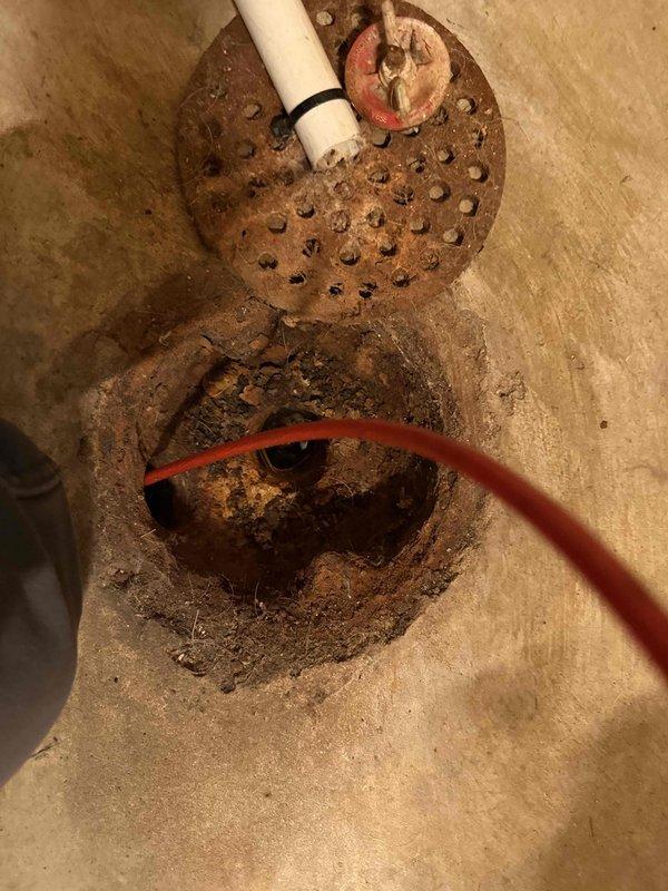 Performed camera inspection of standing drain pipe in basement area to diagnose washing machine drainage backup issue. Accessed the drain system through floor opening, revealing a heavily corroded metal drain cover with significant rust deterioration. Inserted camera equipment to evaluate internal pipe condition and identify potential blockage causing the reported backup problem.