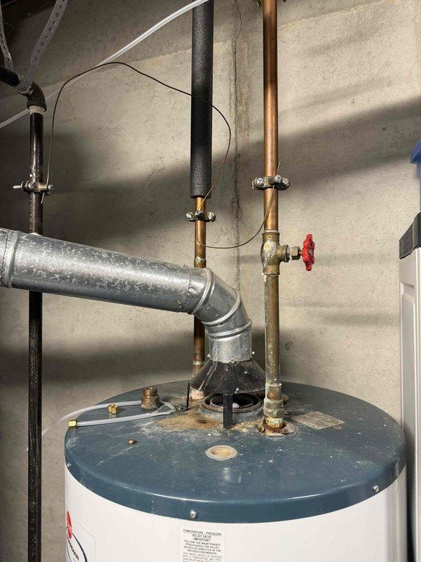 Responded to service call for washing machine drain backup in basement. Upon inspection, determined the issue was not related to the washing machine drain but instead identified problems with the water heater system. Documented the Rheem Guardian "Fury" unit's condition and inspected the piping configuration, noting proper venting and supply line connections were intact and functioning normally.