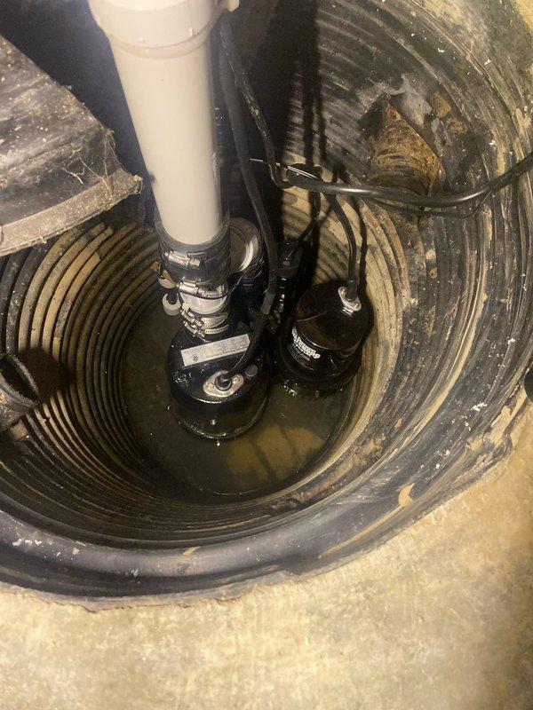 Responded to service call for a non-functioning Basement Watchdog Special Connect battery backup sump pump system that was making a continuous buzzing noise. Upon inspection, found the pump was operational with proper power connection as indicated by the illuminated green LED on the control panel. Verified proper installation of the discharge pipe and pump mechanism within the sump basin, confirming system is now functioning correctly.