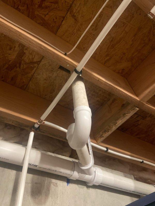 Conducted site assessment for potential installation of US Water Systems softeners/filters. Inspected existing plumbing configuration in utility area, documenting the current PVC pipe layout with horizontal runs near ceiling and vertical sections connecting to main water supply. Evaluated available space and mounting options for new water treatment system installation.