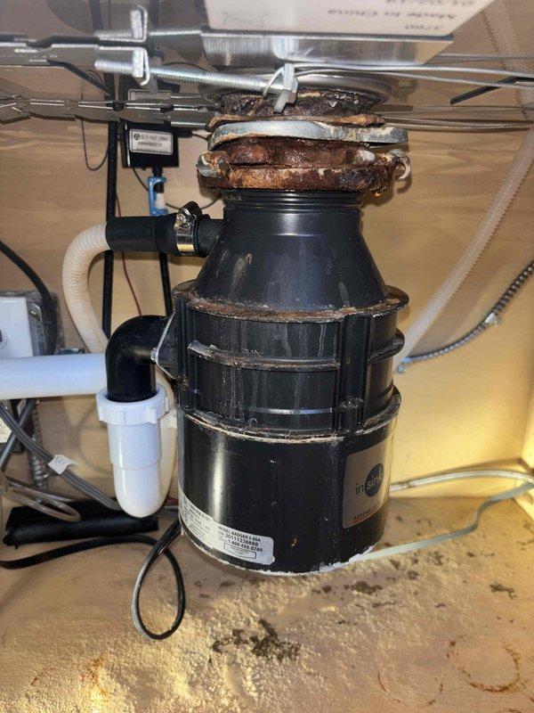 Replaced severely corroded garbage disposal unit at kitchen island sink that was leaking due to rust damage at the flange connection, causing water damage to the cabinet base. Performed additional inspection of reported leaking Kohler Veil Comfort Height toilet in master bathroom.