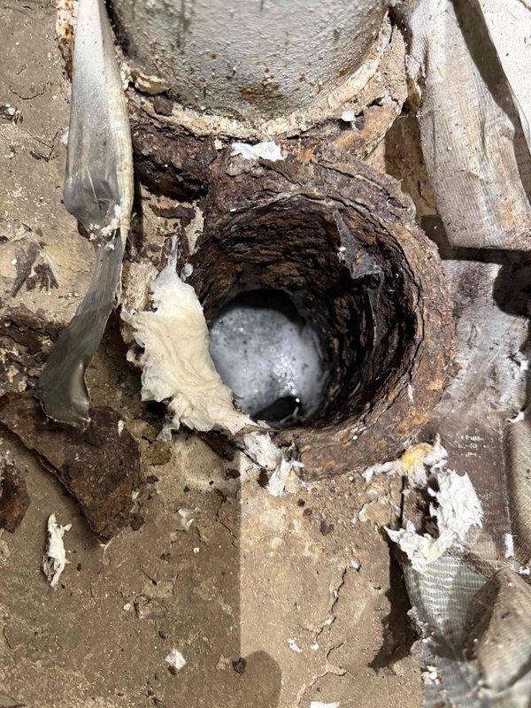 Cleaned main drain line in the basement that was backing up. Visual inspection revealed significant corrosion and deterioration of the drain pipe with standing water present. Successfully cleared blockage and restored proper drainage function.