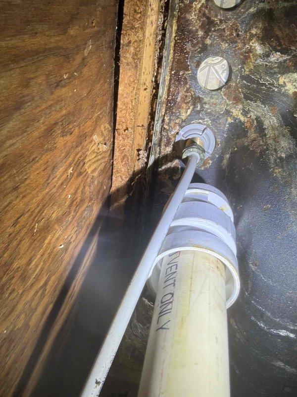 Responded to water leak under kitchen sink. Upon inspection, found significant water damage to wooden structural support beam and surrounding areas with visible deterioration. Observed extensive corrosion on metal surfaces where PVC pipes penetrate, with particular concern around pipe entry points labeled "VENT ONLY" where moisture intrusion was evident.