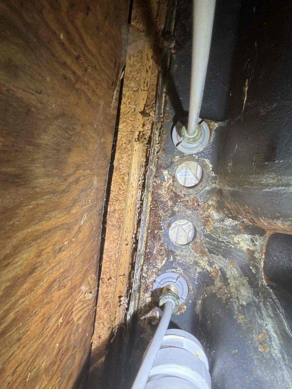 Responded to water leak under kitchen sink. Upon inspection, found significant water damage to wooden structural support beam and surrounding areas with visible deterioration. Observed extensive corrosion on metal surfaces where PVC pipes penetrate, with particular concern around pipe entry points labeled "VENT ONLY" where moisture intrusion was evident.