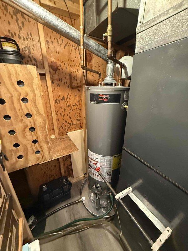 Successfully installed a new 40-gallon Ruud gas water heater with expansion tank in utility room, replacing the previous unit which showed signs of water damage to surrounding surfaces. Installation required two technicians to navigate stairway access constraints, with all connections properly fitted using copper piping and appropriate valves.