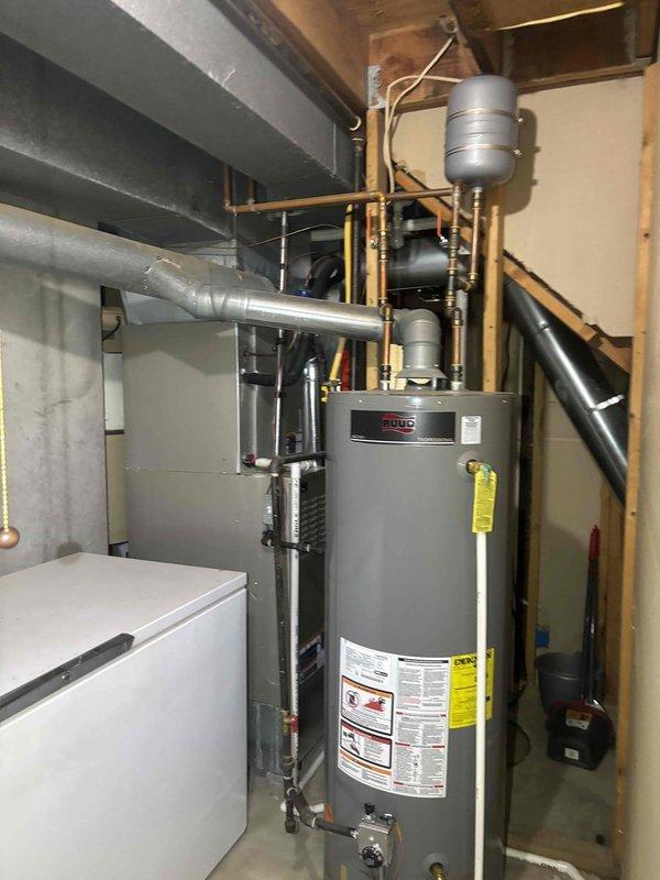 Inspected reported moisture at flute joint on Ruud water heater system. Examined copper pipe connections and PVC fittings throughout the utility room installation. No active leaks detected during inspection; system currently operating normally with all connections secure.