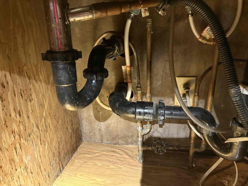 Responded to service call for kitchen sink clogged drain. Inspected P-trap configuration under double basin sink showing significant rust and mineral buildup around drain stoppers. Successfully cleared blockage and restored proper drainage to both basins.