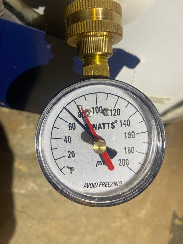 Conducted inspection of 12-year-old basement water heater system. Observed copper pipes showing normal aging with minor corrosion and verified system pressure reading at approximately 80-85 psi on the Watts pressure gauge, which is within acceptable operational range. System remains functional but replacement recommended due to age approaching end of typical service life.