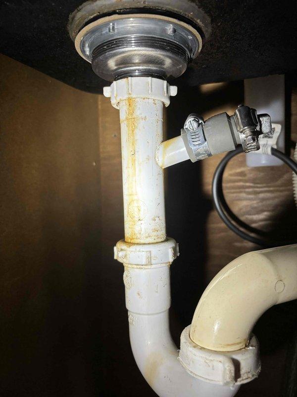Responded to service call for leaking kitchen faucet. Upon inspection, found significant discoloration, rust stains, and mineral deposits on the PVC drain pipe assembly, particularly around the P-trap. Removed old faucet, installed new company-supplied replacement, and verified proper operation with no leaks.